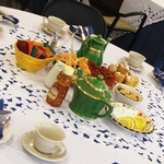 Colorful table display, featuring green teapots, cups and saucers, lemon wedges, tea assortment and finger foods